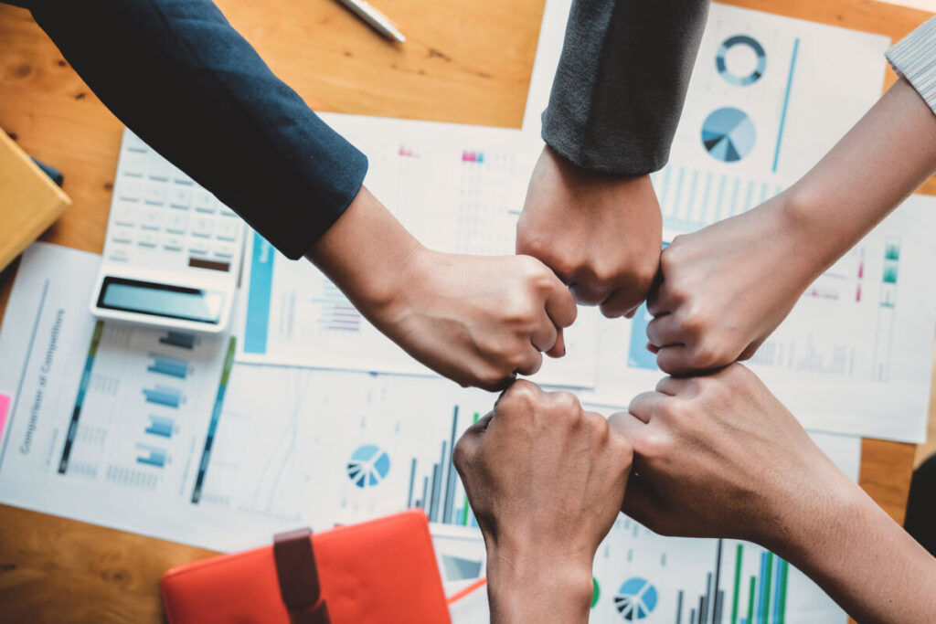 Des mains de professionnels formés en secourisme se réunissent dans un geste symbolique de collaboration, mettant en avant l’importance de la formation et du travail d’équipe.